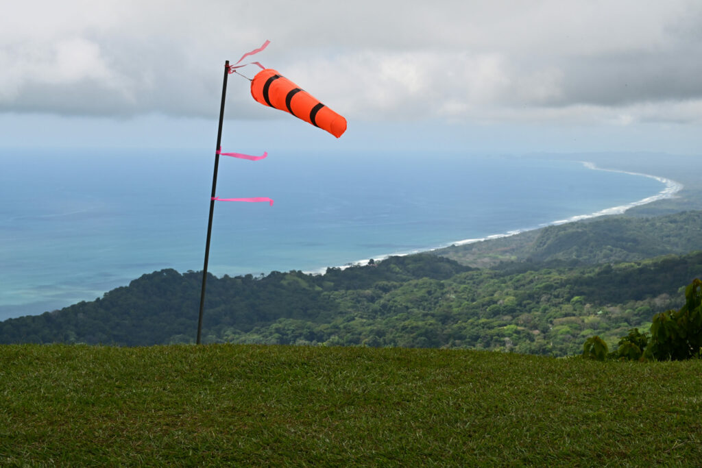 Wind sock in the foreground with jungle, shoreline and clouds in the background