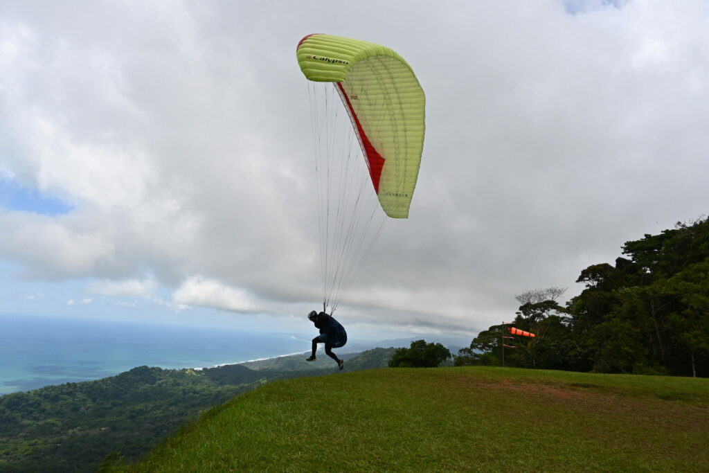 Paraglider taking off from a green grass area, huge clouds and the sea in the back