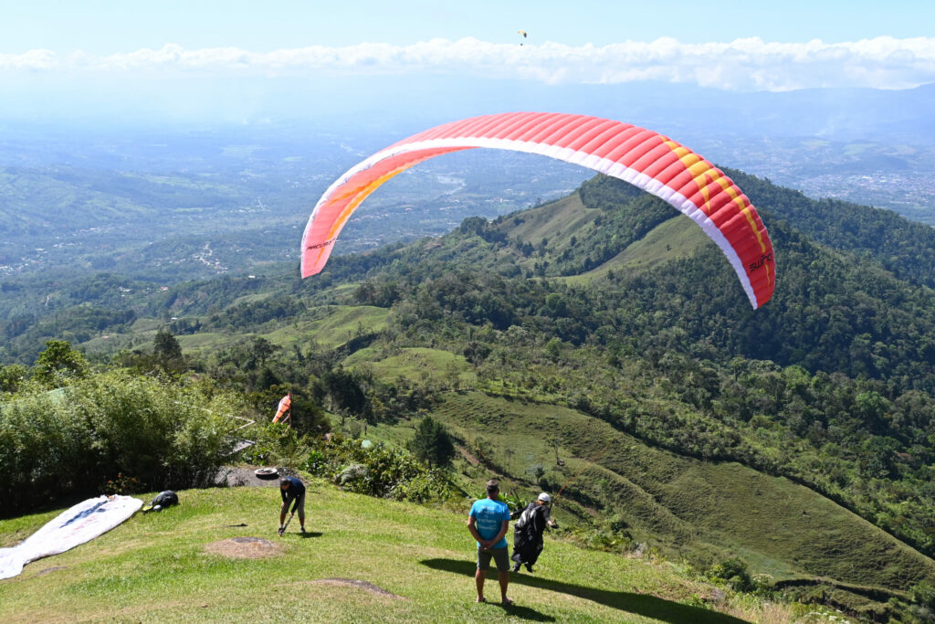 Paraglider at takeoff with a green mountain range in the background