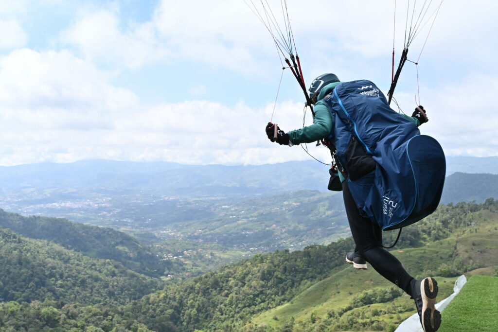 Paragliding pilot taking off from a platform launching into a green valley