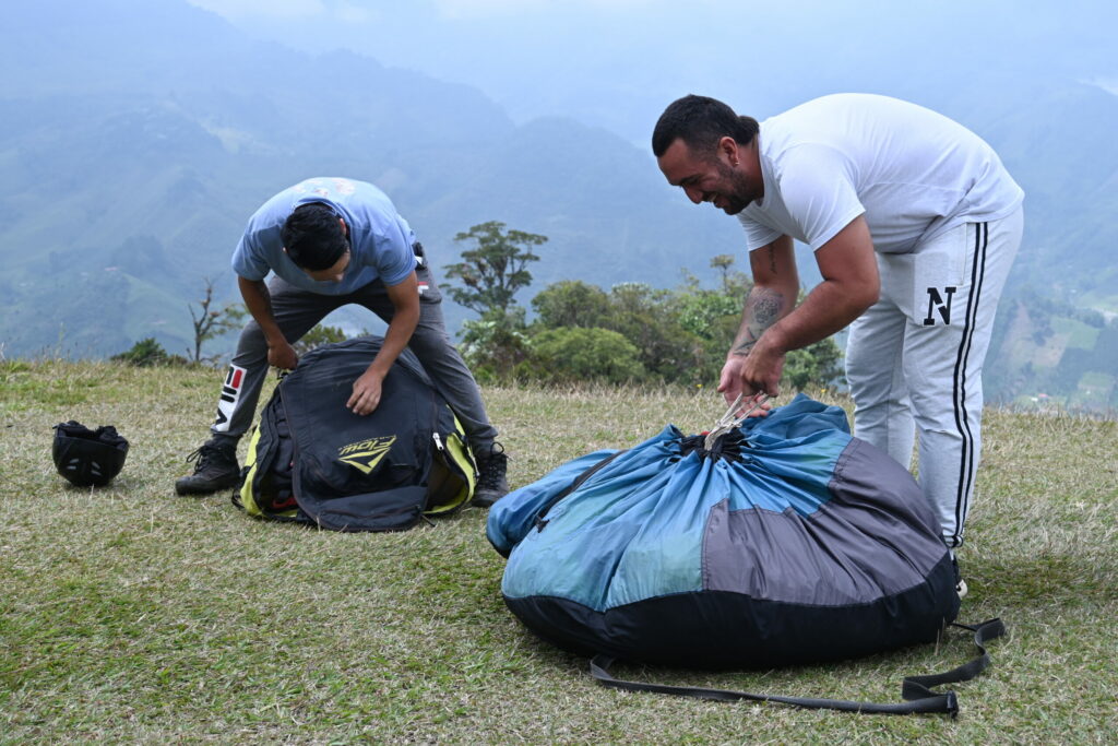 Two paragliding tandem pilots unpacking their equipment while chatting with each other