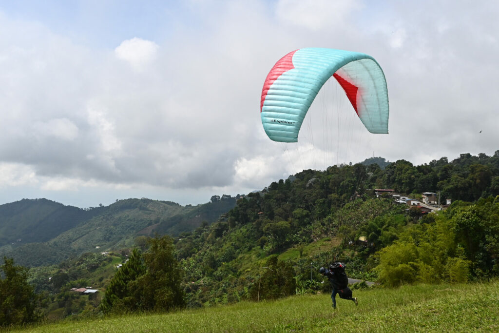 Paraglider taking off from a green hillside with a ridge and cloud in the background