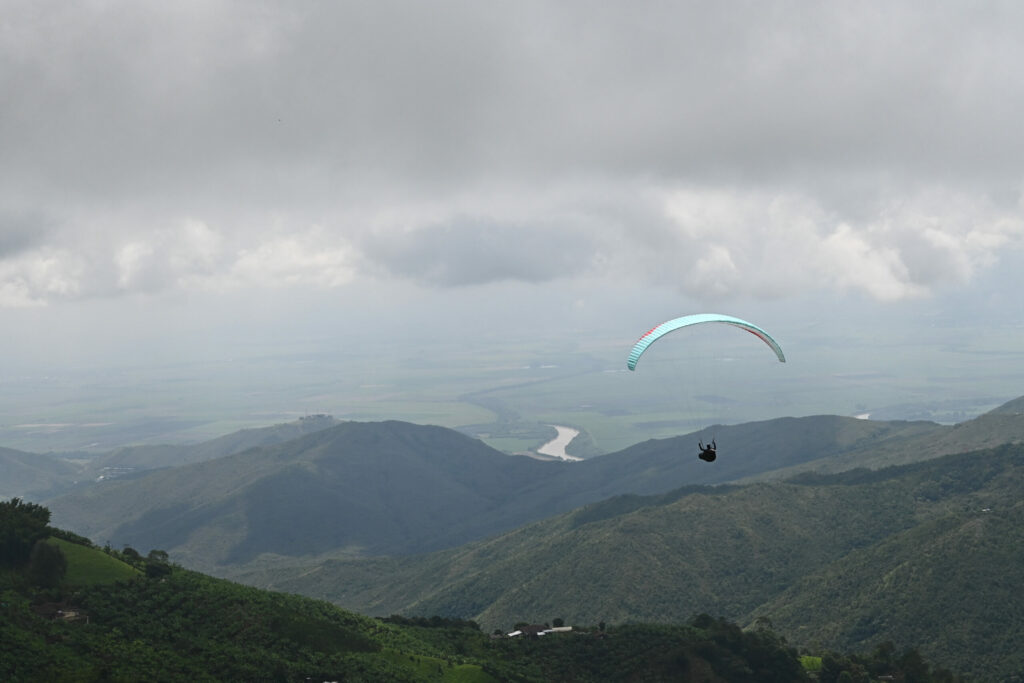 Paraglider in the foreground with a valley and river in the background and gray clouds above