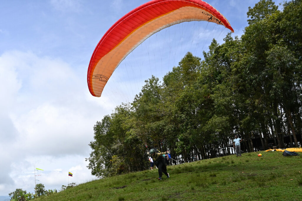 A paraglider during takeoff on a green hillside with trees in the background